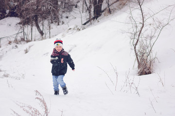 Fototapeta na wymiar Little smiling boy plays and runs on the street in snowy winter