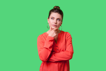 Need to think! Portrait of pensive elegant young woman with bun hairstyle, big earrings and in red...