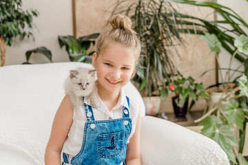 Little cute girl with kitten on sofa at home. portrait of a child with a kitten