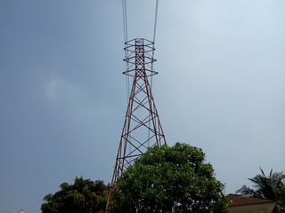 Photo of an electrical transmission tower and electrical lines with blue sky background and trees - Image