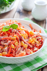 Salad with fresh carrots, sausage and corn on a white plate, selective focus