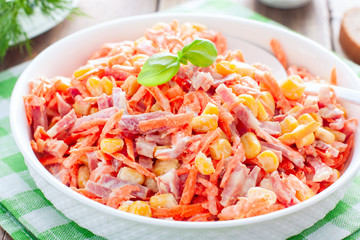 Salad with fresh carrots, sausage and corn on a white plate on a wooden table, horizontal