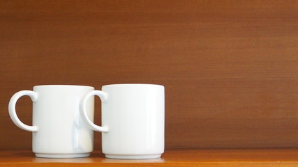 Two stacking white porcelain mugs on wooden shelf in the kitchen. Living and lifestyle concept. Home decoration and display