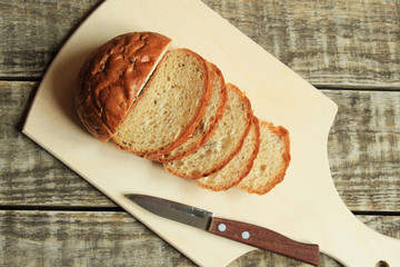 Sliced ​​bread lies on a wooden board. Nearby lies a knife.