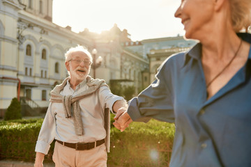 Come with me. Beautiful and happy elderly couple holding hands and smiling while spending time together outdoors on a sunny day