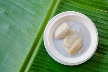 Close up and top view : Banana in coconut milk (Thai popular dessert) in white bowl on green banana leaf background.