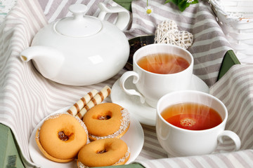 Two cups of hot tea with delicious cookies on white wooden table