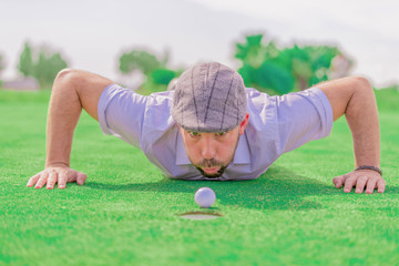 Portrait of a man with a beard and a grey cap, trying to move a white golf ball blowing, with the...