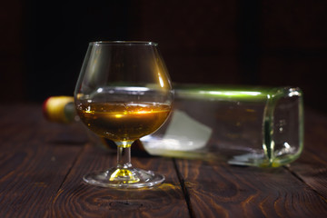 Glass of whiskey or brandy and empty bottles on wooden table
