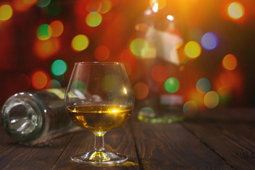 Glass of whiskey or brandy and empty bottles on wooden table on bright glowing background