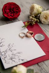 Red wedding. Wedding rings on white and red invitation near red flowers
