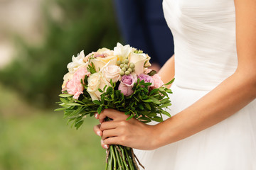 Obraz na płótnie Canvas Bride in beautiful white wedding dress holding bouquet of fresh flowers at her happy wedding day
