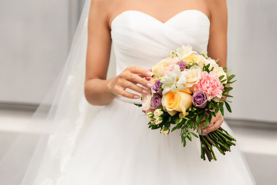 Bride in beautiful white wedding dress holding bouquet of fresh flowers at her happy wedding day