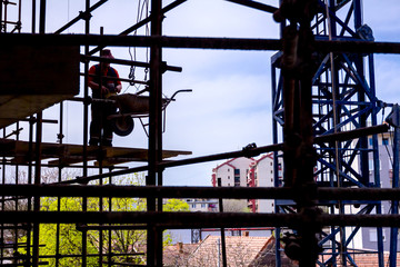 Worker is helping crane to manage wheelbarrow on scaffold