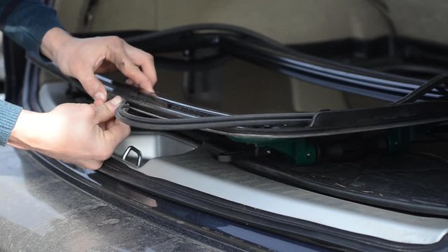 Install sealing gum on the sunroof in the car. Close-up of male hands replacing an elastic band on a hatch in a car.