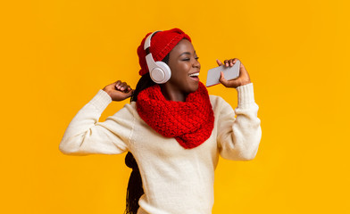 Fototapeta na wymiar Joyful black girl in headphones listening to music and singing