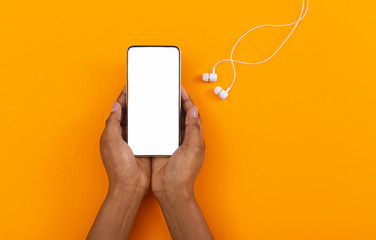 Blank smartphone in female hands and earphones on orange background