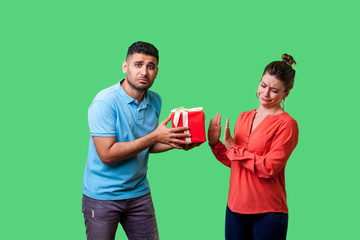 Portrait of upset resentful man in casual clothes giving present to naughty beautiful woman,...