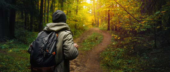 A man with backpack walks in the amazing autumn forest. Hiking alone along autumn forest paths. Travel concept. - obrazy, fototapety, plakaty