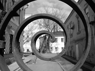 travel photography, metal textured spiral, architecture element front view, black and white with a view of city houses, street, depth of field, close up, macro