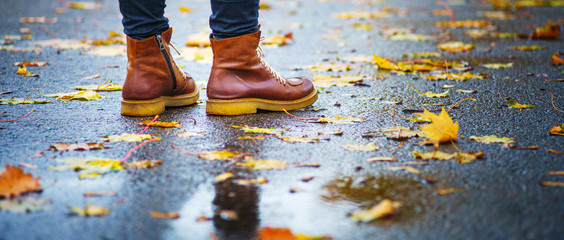 Walk on wet sidewalk. Back view on the feet of a woman standing on the asphalt pavement with...