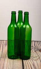 Three empty green glass wine bottles on a wooden table.