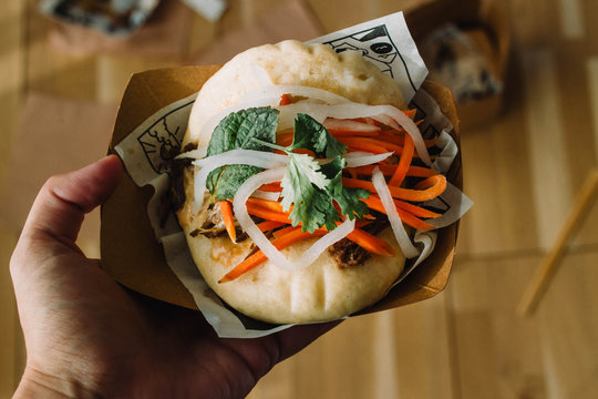 Hand holding gua bao, hirata buns, bao buns, guabao or baozi (traditional asian sandwich). Chinese food from Fuzhou, named Cha bao in Hong Kong and kakuni manju in Japan. Flatlay instagram style 