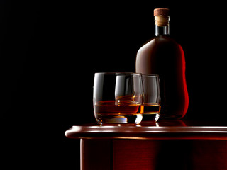 Two glasses of whisky and a full, closed bottle of whisky on a wooden table in a low key.