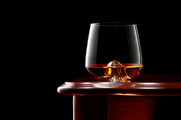 A glass of whiskey on a wooden table in a low key.