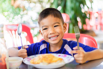 Portrait image of happy Asian child boy eating omelette with rice in the breakfast meal. A child 5 years old.