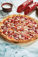 Homemade baked meat pizza with tomatoes, cheese, sausages, red sauce. Composition with crispy pizza, tomatoes on a light background. Copy space. Top view