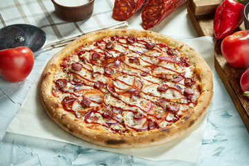 Homemade baked meat pizza with tomatoes, cheese, sausages, red sauce. Composition with crispy pizza, tomatoes on a light background. Copy space. Top view