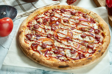 Homemade baked meat pizza with tomatoes, cheese, sausages, red sauce. Composition with crispy pizza, tomatoes on a light background. Copy space. Top view