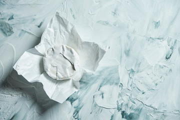 Obraz premium Camembert cheese head on white paper on a light texture background. Top view with copy space. Farm product