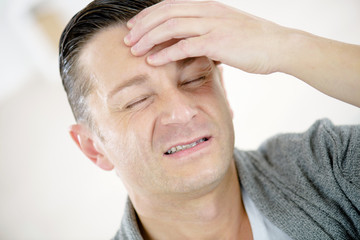 Fototapeta premium closeup of man grimacing and holding his head in pain