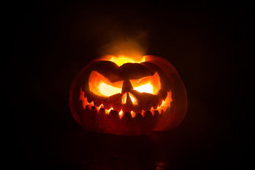 Close up view of scary Halloween pumpkin with eyes glowing inside at black background. Selective...