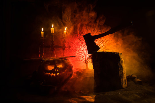 Scary orange pumpkin with carved eyes and a smile with burning candles and an ax