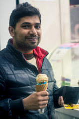 Young indian man in black and red jacket eating ice cream from an open eatery in a shopping mall