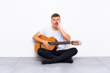 Young handsome man with guitar shouting with mouth wide open