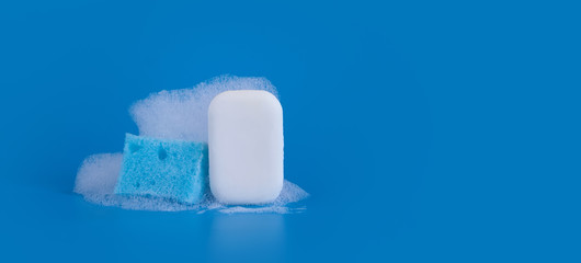 White soap with blue cleaning sponge and soapy bubbles foam on blue background. Copy space.