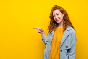 Redhead woman over isolated yellow background pointing finger to the side