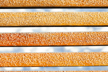 Cold winter weather snow covered bench. Close-up frosted surface snowflakes on wooden background....
