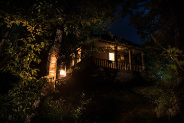 Fototapeta na wymiar Old house with a Ghost in the forest at night or Abandoned Haunted Horror House in fog. Old mystic building in dead tree forest. Trees at night with moon. Surreal lights. Horror Halloween concept