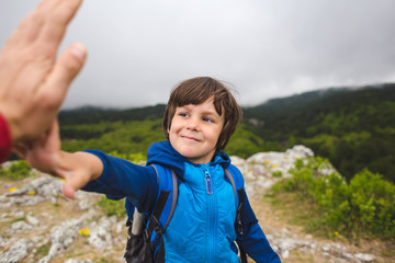 A boy with a backpack climbed to the top of the mountain and gives five.