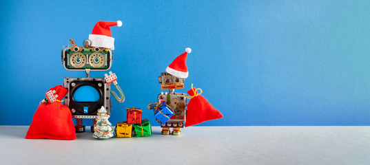 Two Santa Claus steampunk toys on blue background. Festive Christmas New year greeting card mockup with funny robots dressed red Santa hat. Mockup blue screen display, empty space backdrop for text