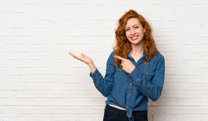 Redhead woman over white brick wall holding copyspace imaginary on the palm to insert an ad