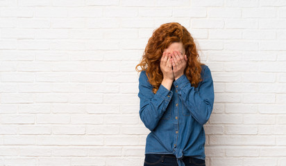 Redhead woman over white brick wall with tired and sick expression