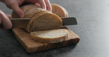 man hand slicing ciabatta on olive board