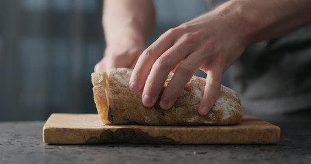 man hand slicing ciabatta on olive board
