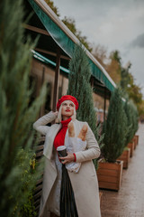 Nice young girl in white coat and red beret joy and happy. Walking near city cafe with baguettes ..